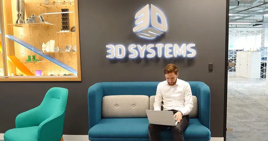 Un hombre sentado en una salón de 3D Systems, trabajando en su computadora portátil