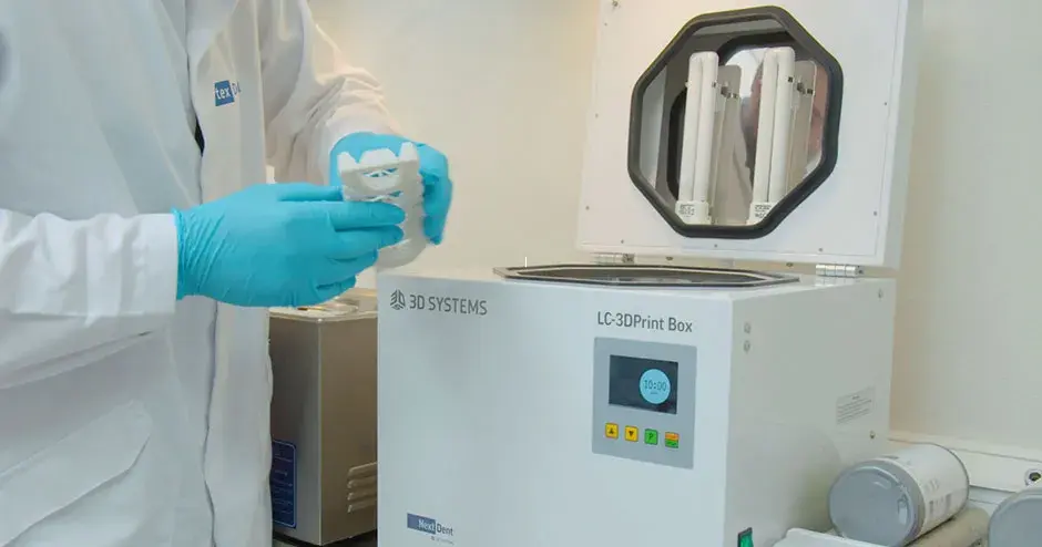 Una persona sosteniendo una prótesis dental extraída de una máquina de postprocesamiento