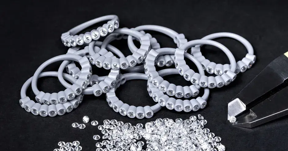 muchos anillos moldeados en cera con diamantes engastados, punta de pinza sosteniendo un diamante, diamantes dispersos